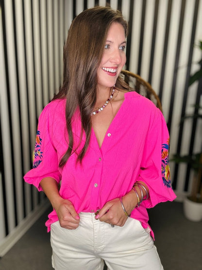 Woman wearing a bright pink blouse with colorful sleeves indoors.