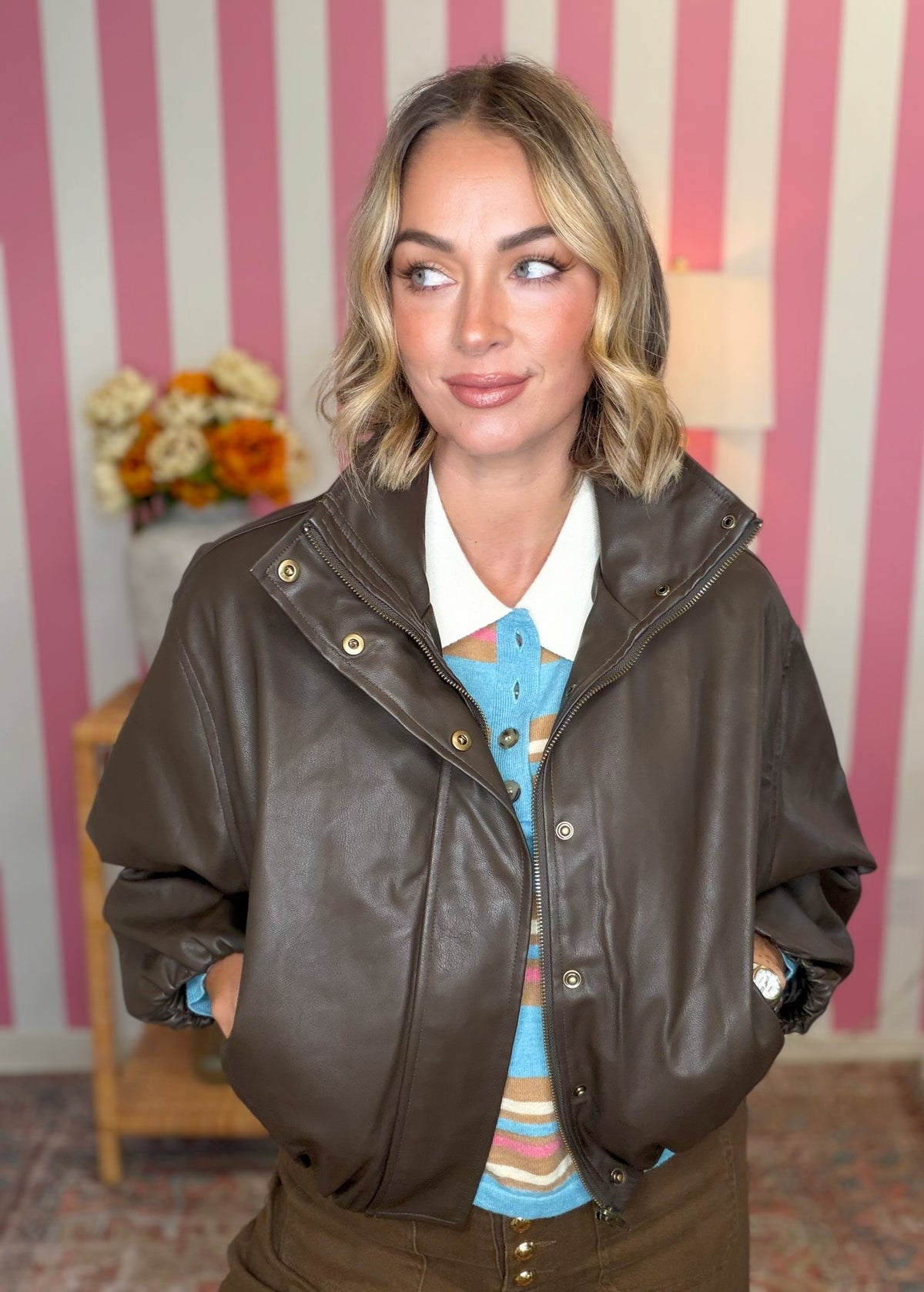 woman standing in an espresso colored leather jacket with a blue striped polo underneath