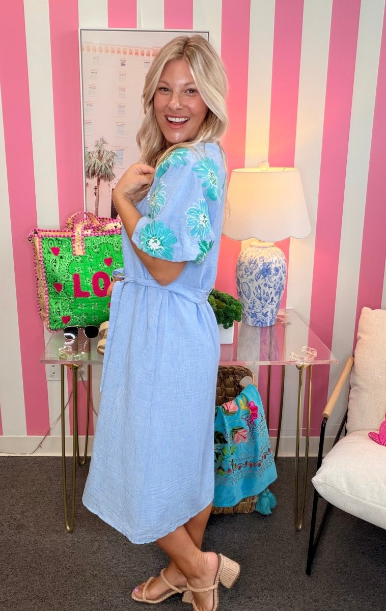 Woman in a light blue dress standing in a room with pink and white striped walls.