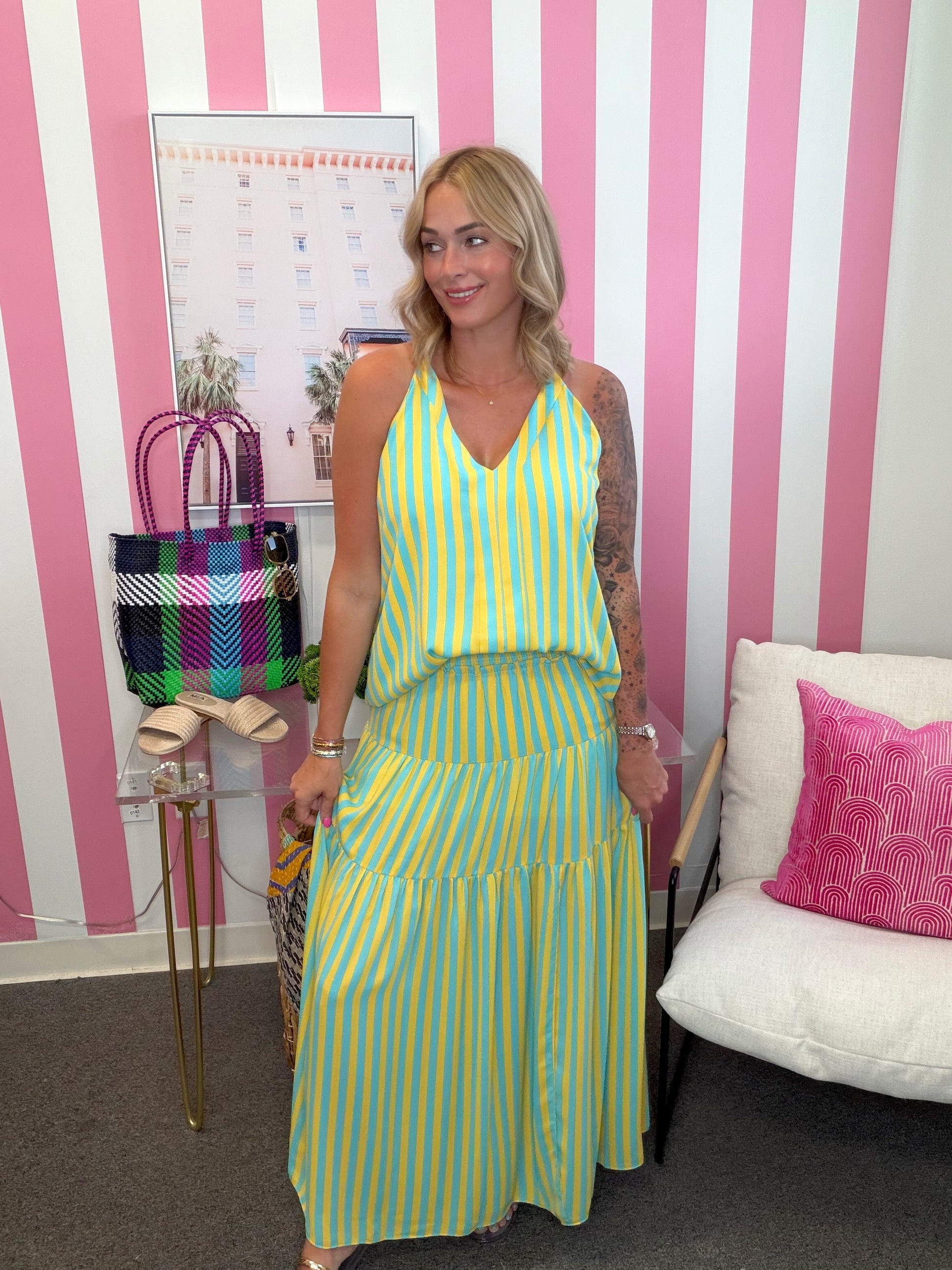 Woman in a yellow and green striped dress standing in a room with pink and white striped walls.