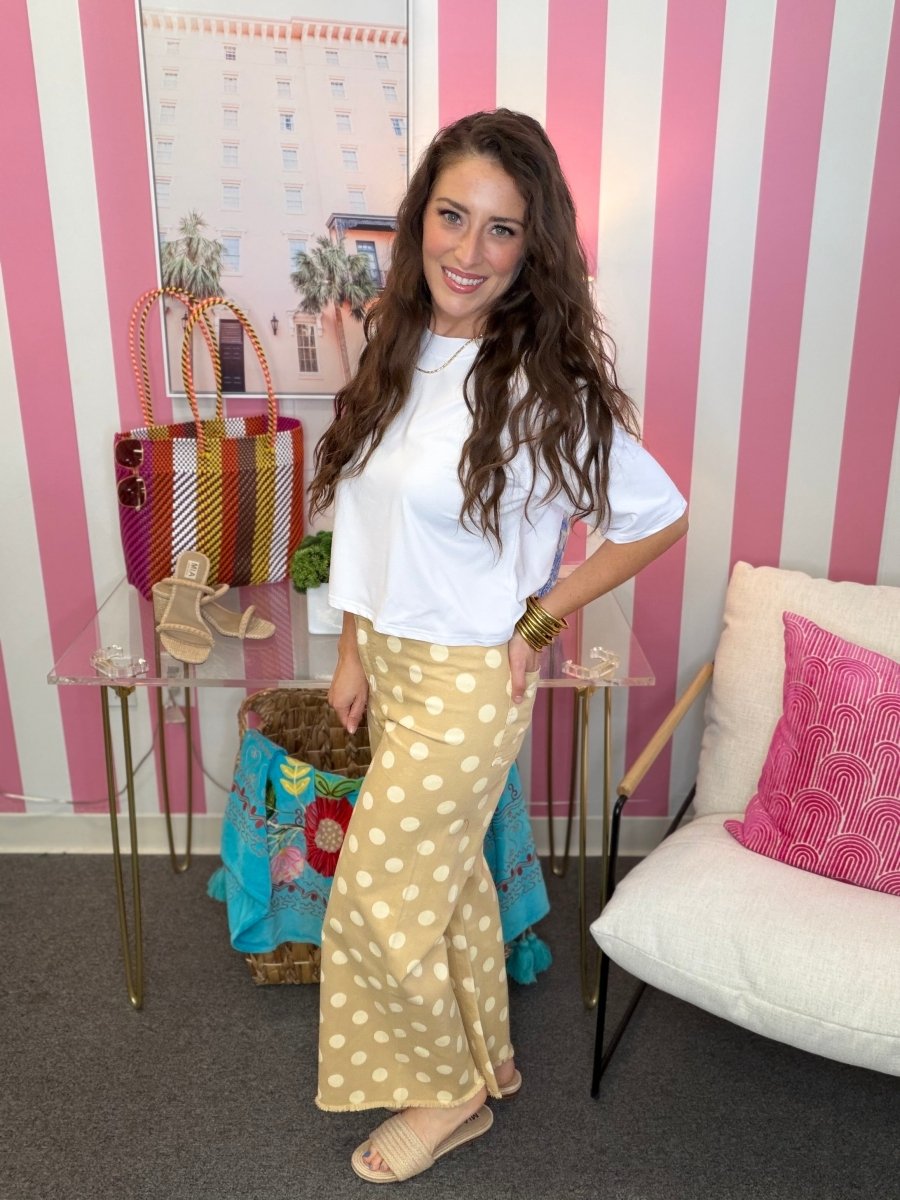 Woman in a white top and yellow polka dot pants standing in a room with striped walls and a chair.