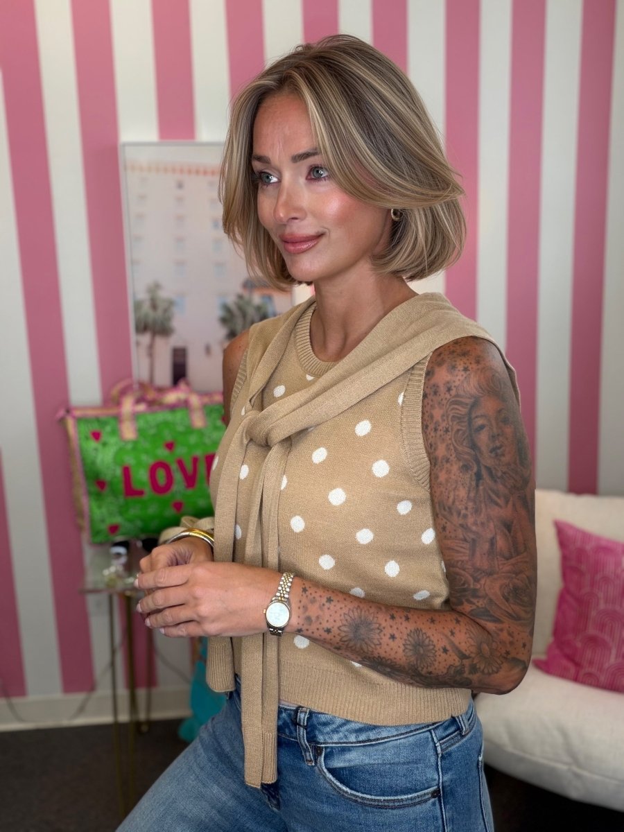 Woman wearing a beige sleeveless polka dot top with a scarf in a room with pink and white striped walls.