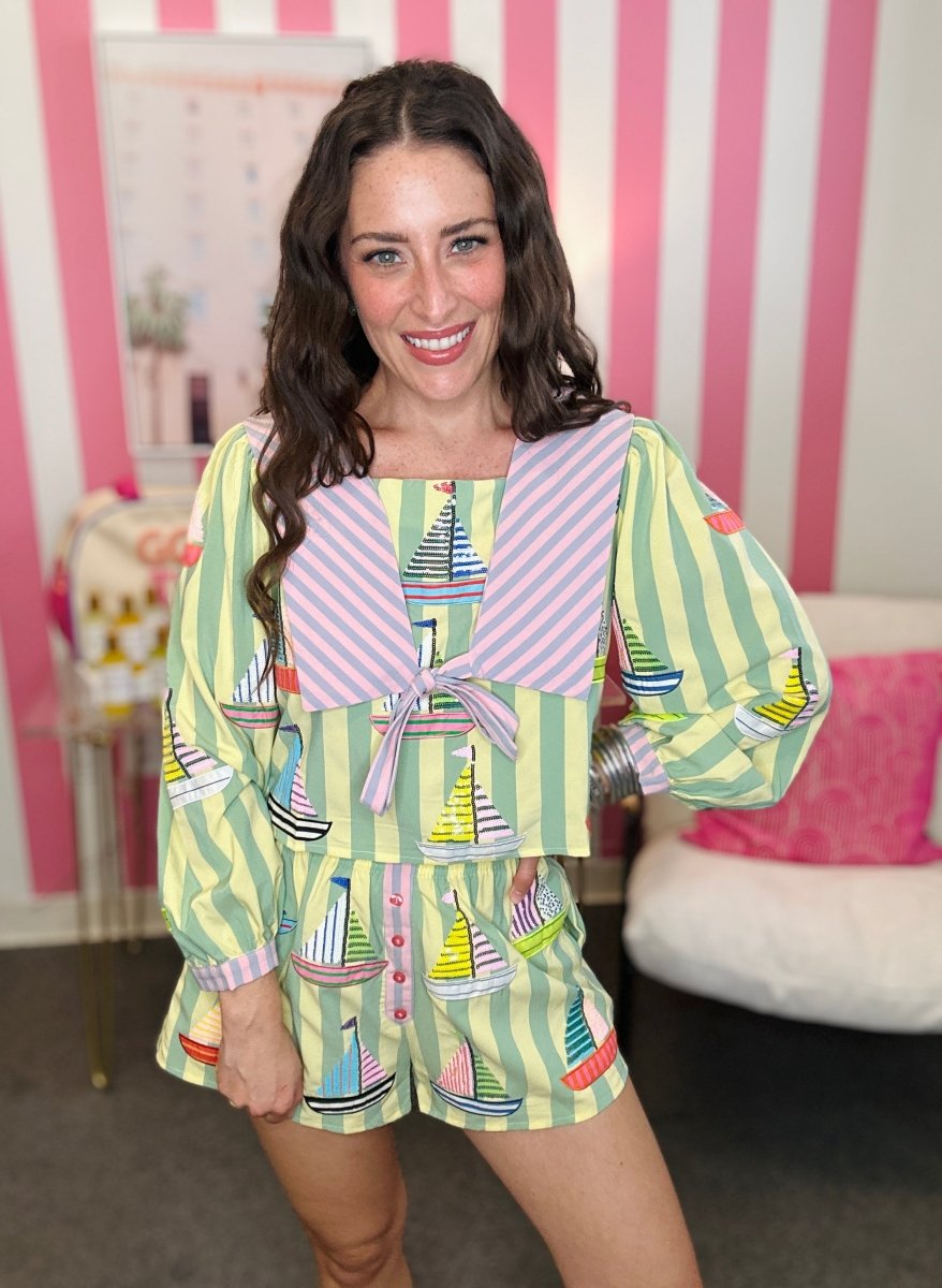 Woman wearing a colorful outfit with sailboat patterns in a room with pink and white striped curtains.
