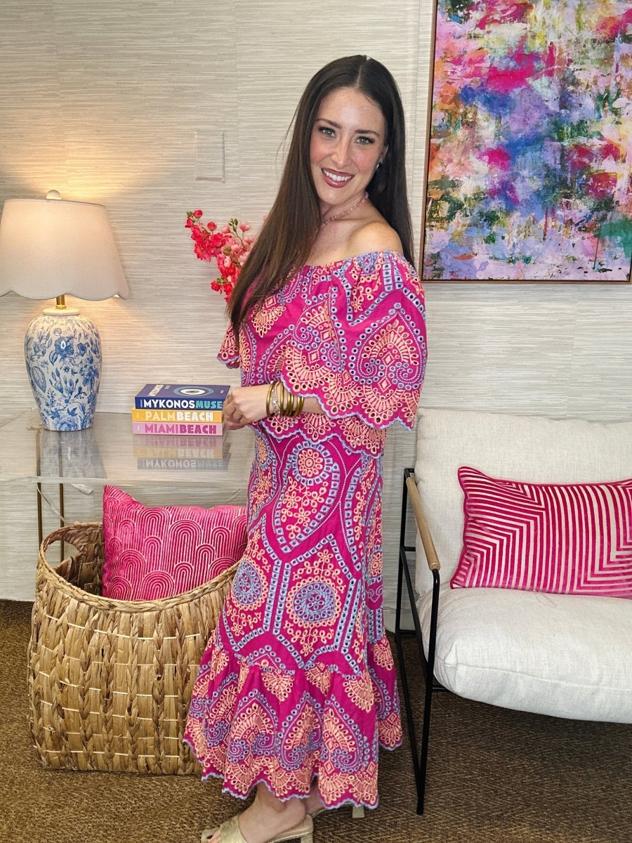 Woman in a colorful dress standing in a living room with a couch and decorative pillows.