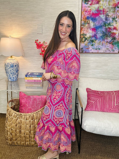 Woman in a colorful dress standing in a living room with a couch and decorative pillows.