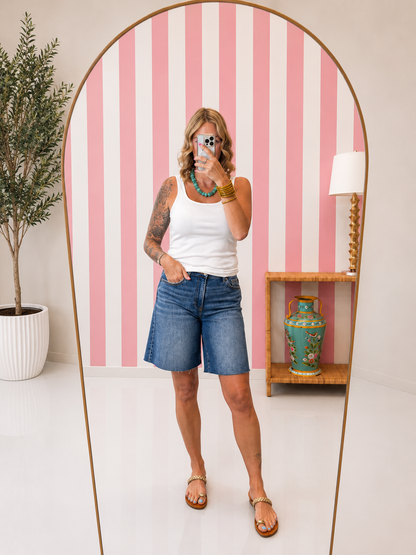Woman taking a mirror selfie in a room with pink and white striped wallpaper.