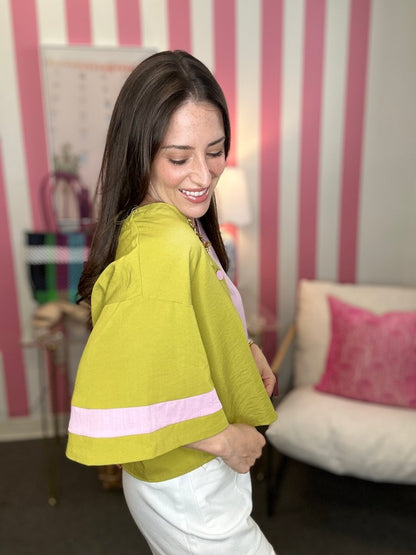 Woman wearing a green jacket with a pink stripe in a room with striped walls and a white couch.