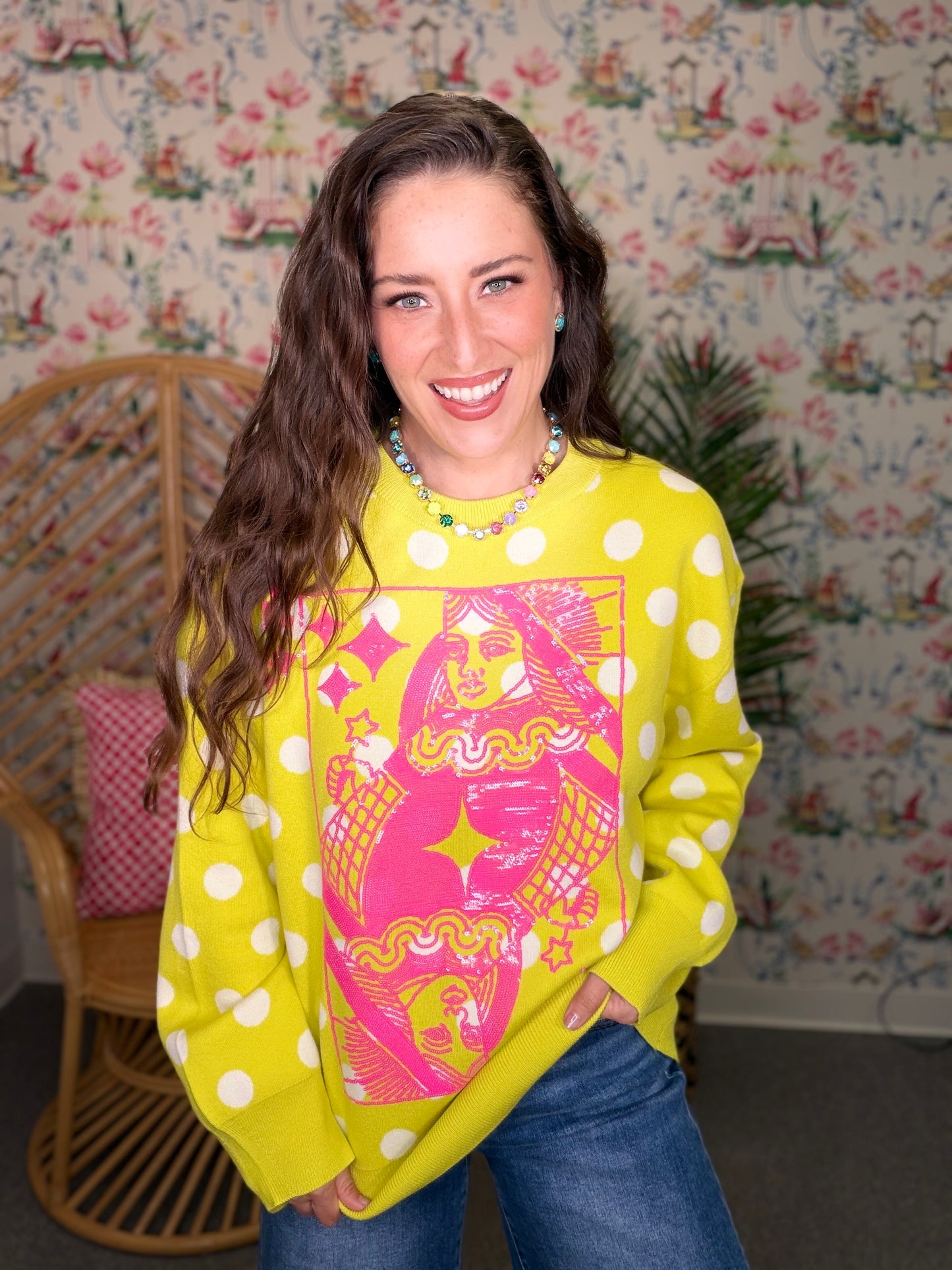 Woman wearing a bright yellow sweatshirt with a colorful graphic design in a room with floral wallpaper.