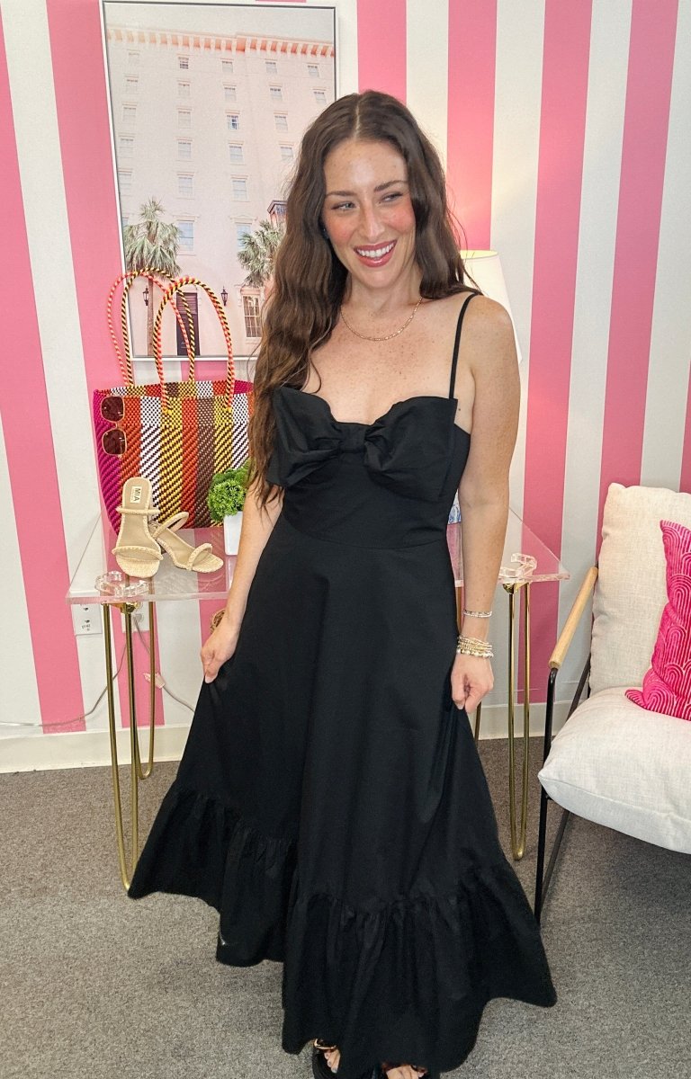 Woman in a black dress standing in a room with pink and white striped walls.