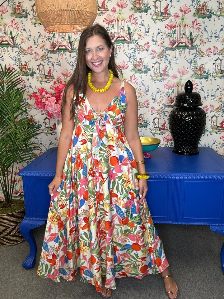 Woman in a colorful dress standing on a patterned rug with a blue box and decorative items around.