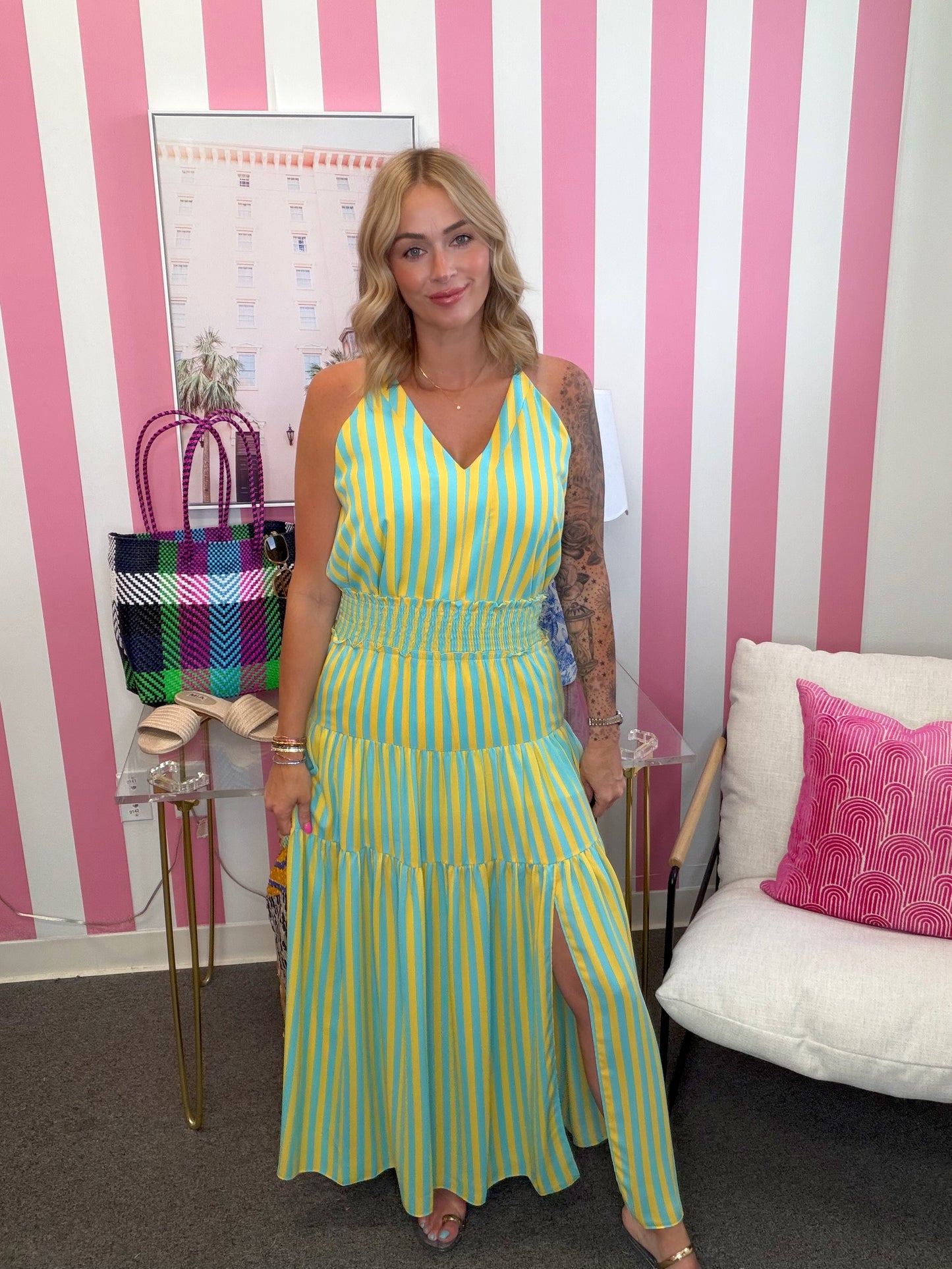 Woman in a yellow and green striped dress standing in front of a pink and white striped wall.