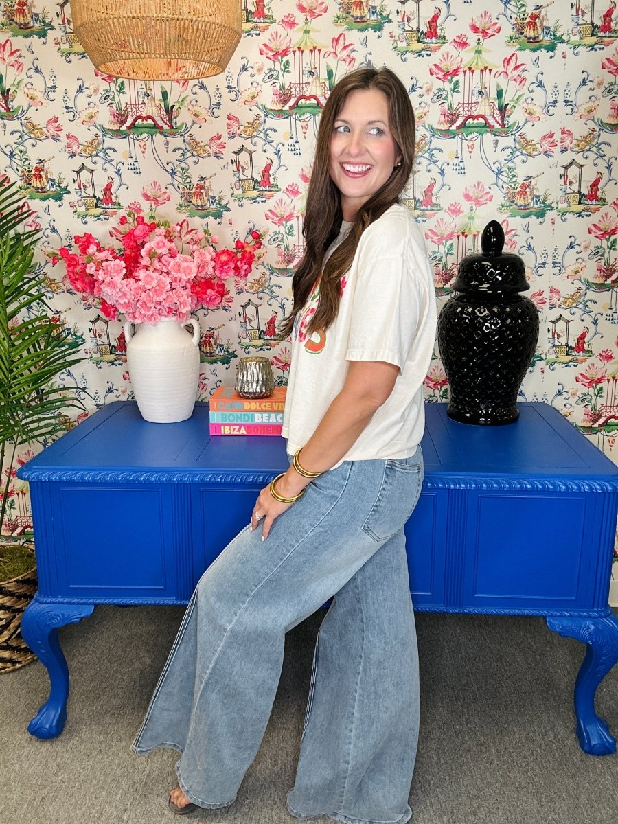 Woman posing in front of a colorful wall with floral arrangements and a blue table.