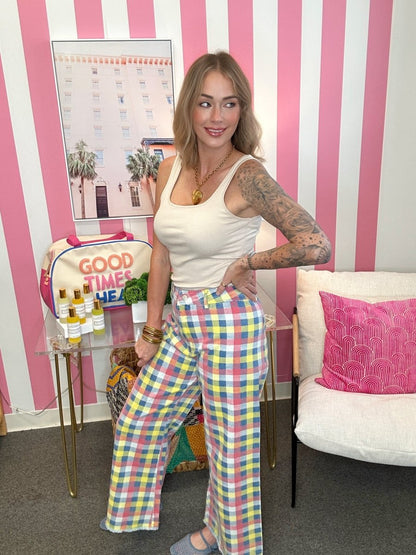 Woman in a white tank top and colorful plaid pants standing in a room with pink and white striped walls.