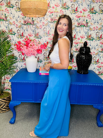 Woman in a blue dress standing next to a blue table with decorative items against a patterned wall.
