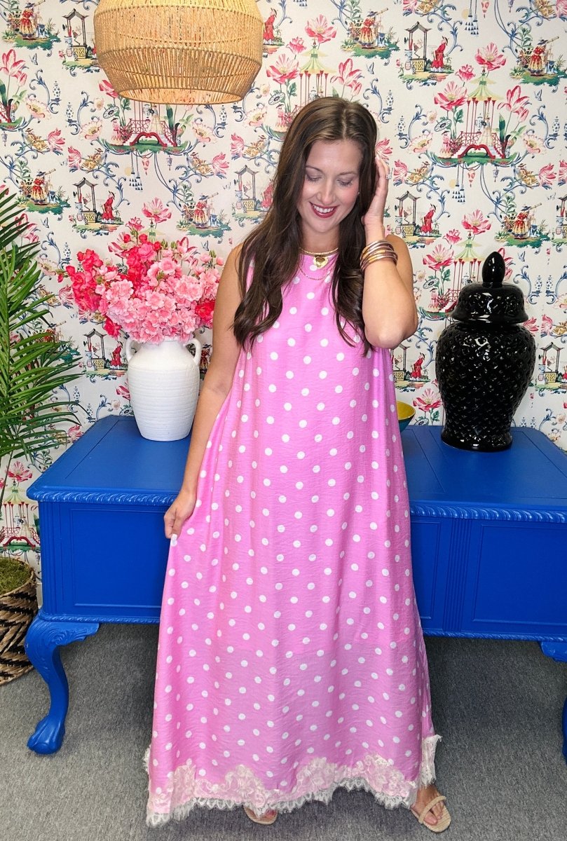 Woman in a pink polka dot dress standing in a room with colorful wallpaper and furniture.