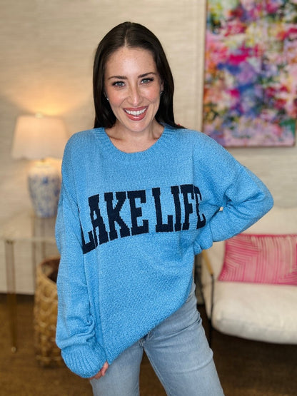 Woman wearing a blue 'LAKE LIFE' sweater in a living room setting.