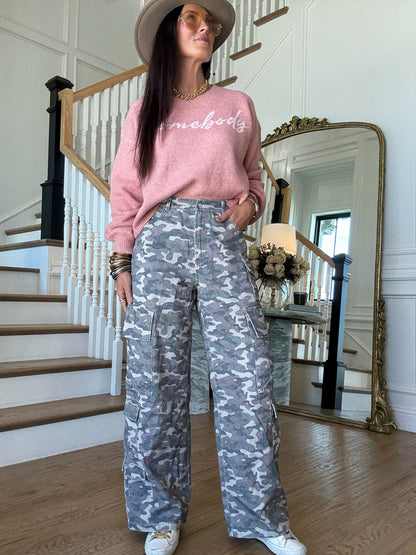 woman standing in a pink sweater and camo cargo pants