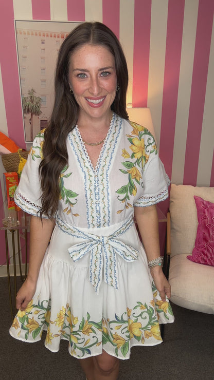 Woman wearing a white dress with floral patterns in a room with striped walls.