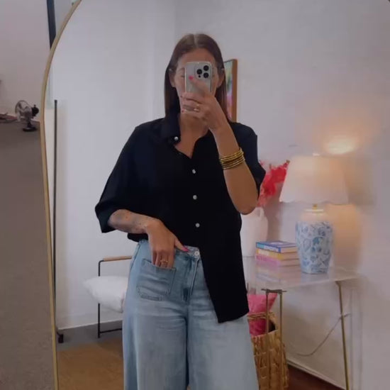 Woman wearing a black shirt and blue jeans standing in front of a mirror.