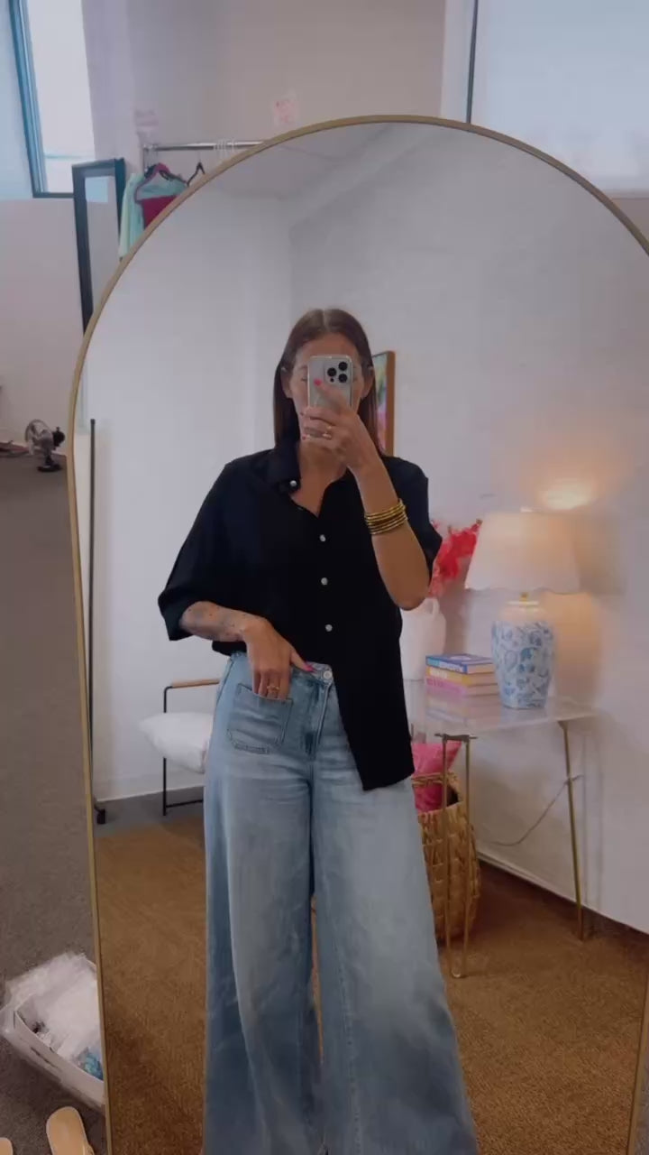 Woman wearing a black shirt and blue jeans standing in front of a mirror.