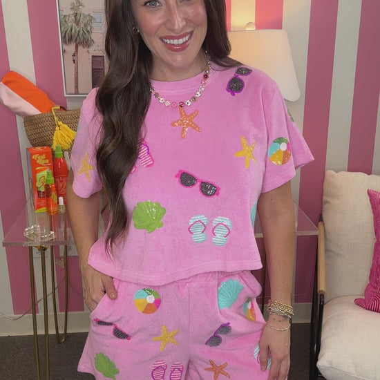Woman wearing a pink pajama set with beach-themed designs in a room with striped walls.