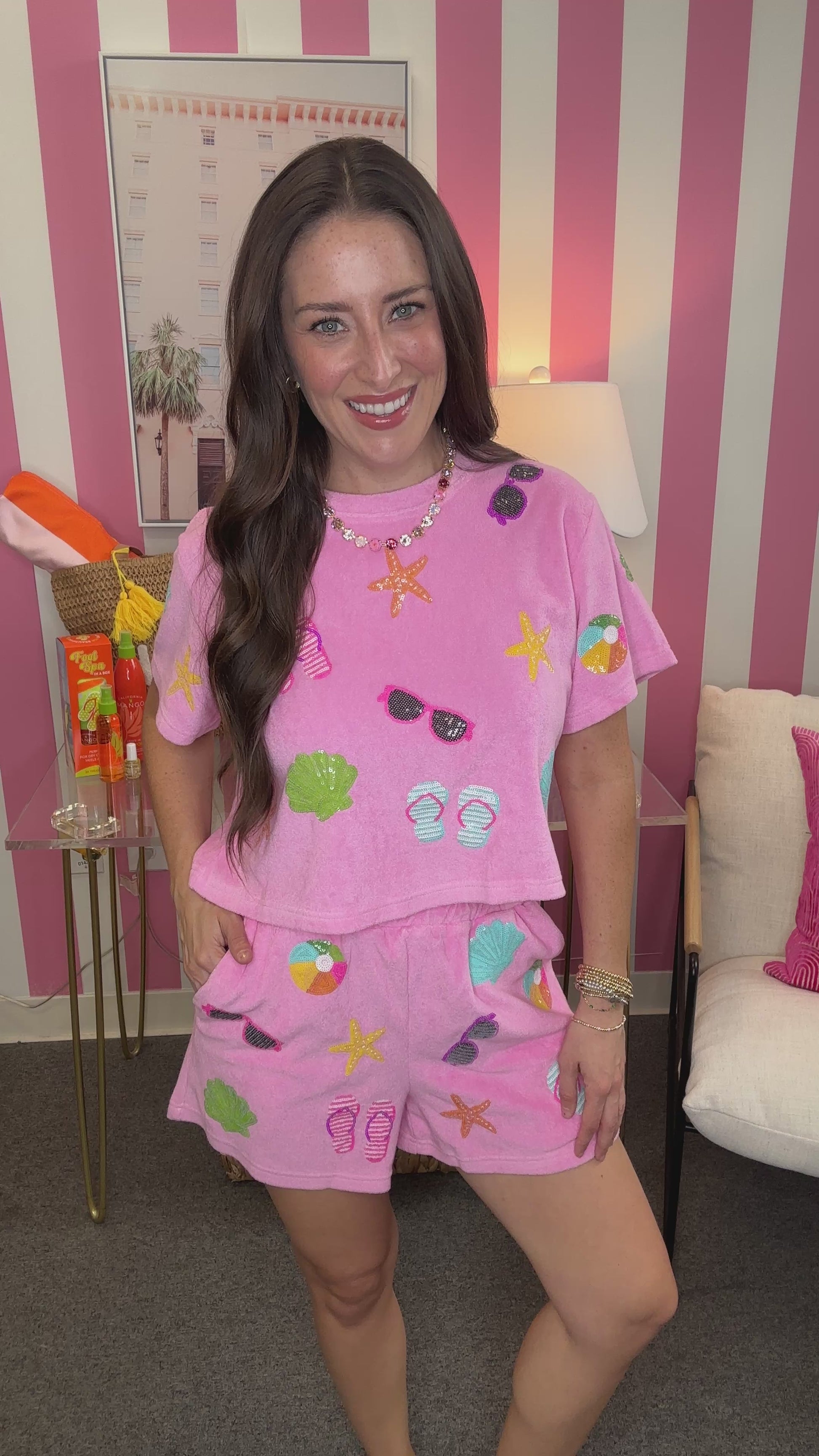 Woman wearing a pink pajama set with beach-themed designs in a room with striped walls.