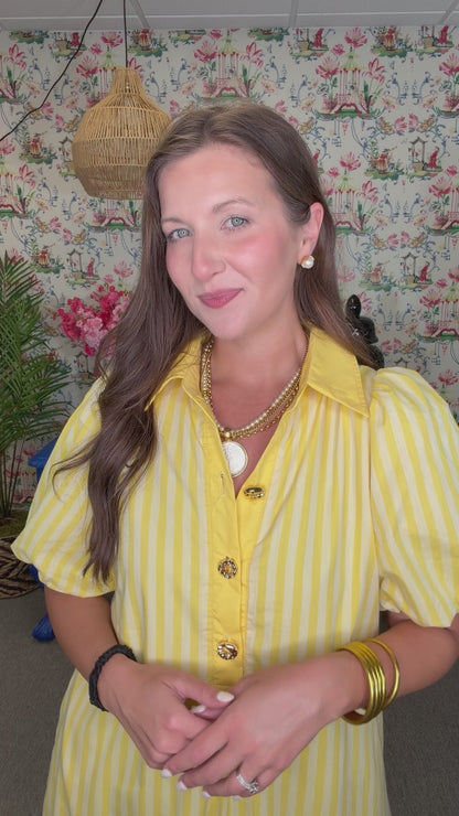 Woman in a yellow dress standing in front of a colorful wall with floral patterns.