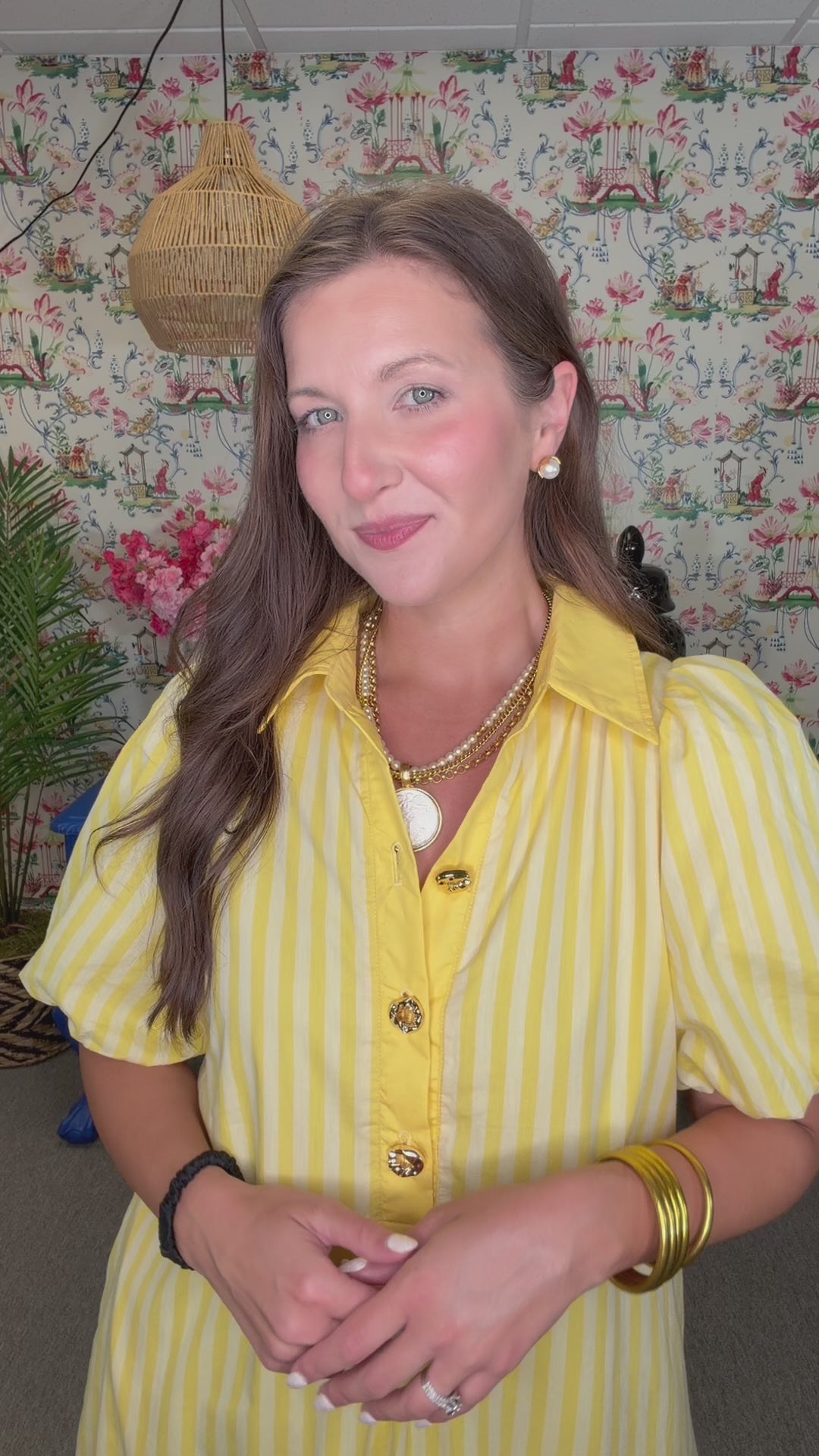 Woman in a yellow dress standing in front of a colorful wall with floral patterns.