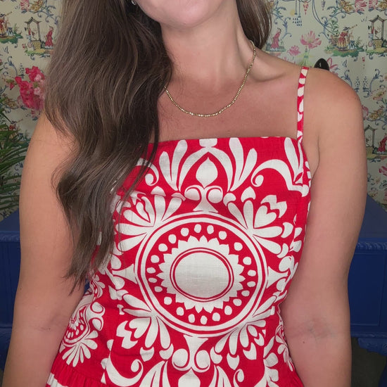Woman in a red and white dress standing in front of a colorful wall with floral arrangements and a blue table.
