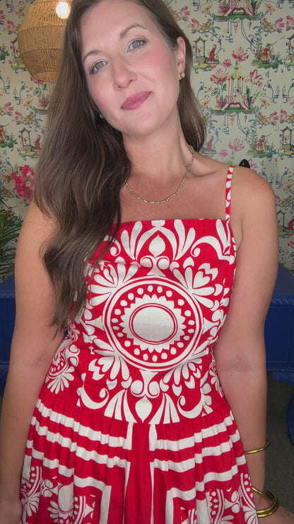 Woman in a red and white dress standing in front of a colorful wall with floral arrangements and a blue table.
