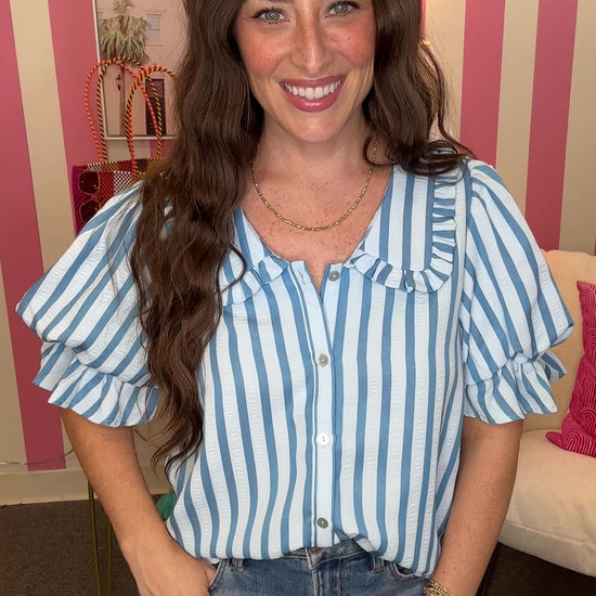 Woman wearing a blue and white striped shirt with ruffled sleeves in an indoor setting.