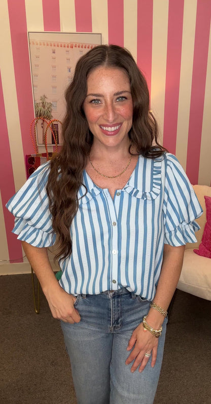 Woman wearing a blue and white striped shirt with ruffled sleeves in an indoor setting.