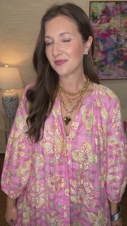 Woman in a pink floral dress standing in a room with a lamp and colorful painting.