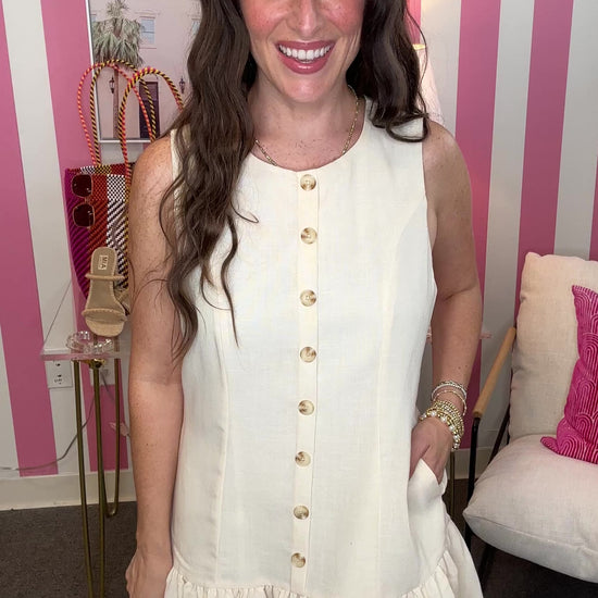 Woman wearing a white dress with gold buttons in a room with pink and white striped walls.