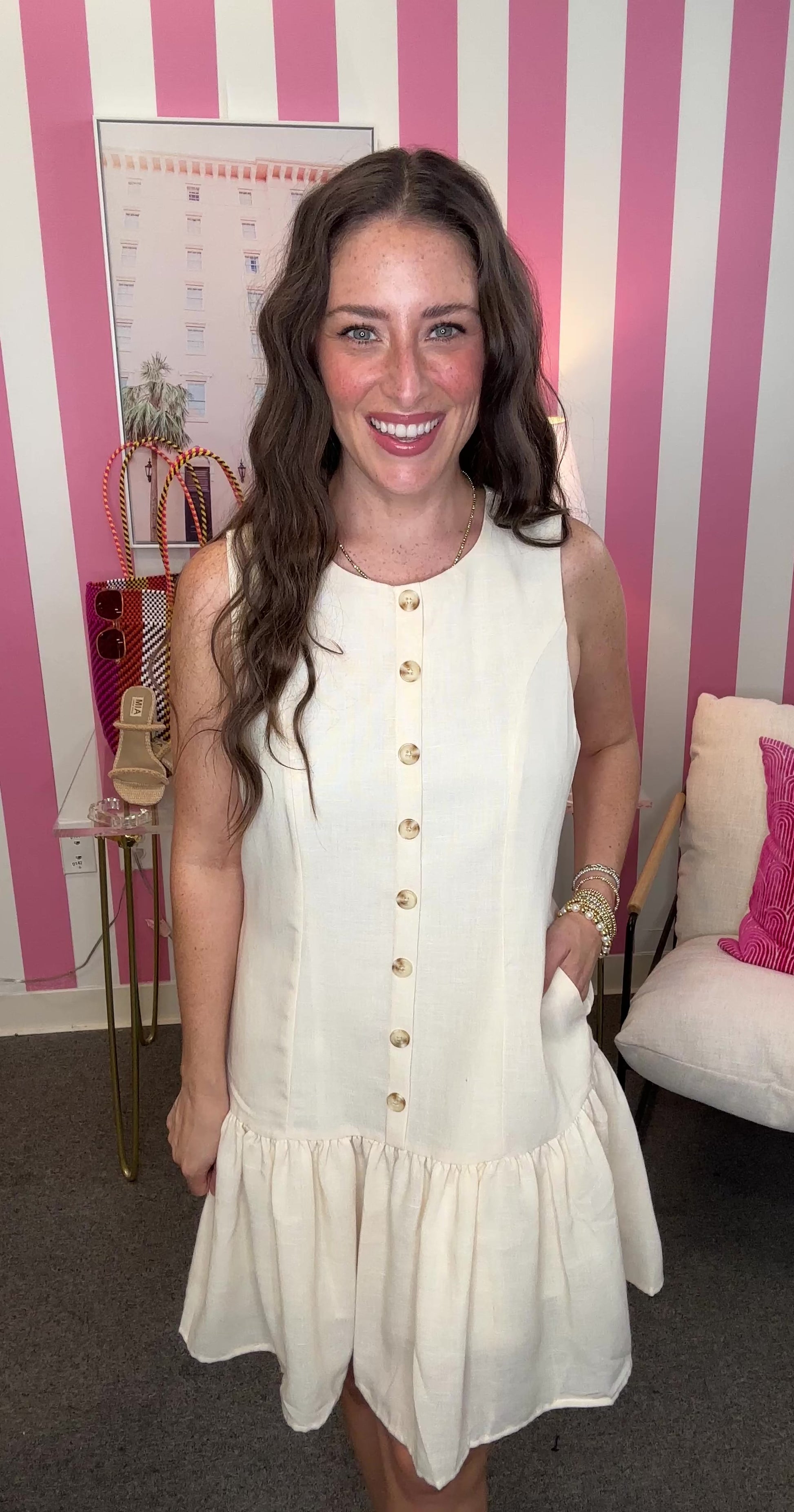 Woman wearing a white dress with gold buttons in a room with pink and white striped walls.