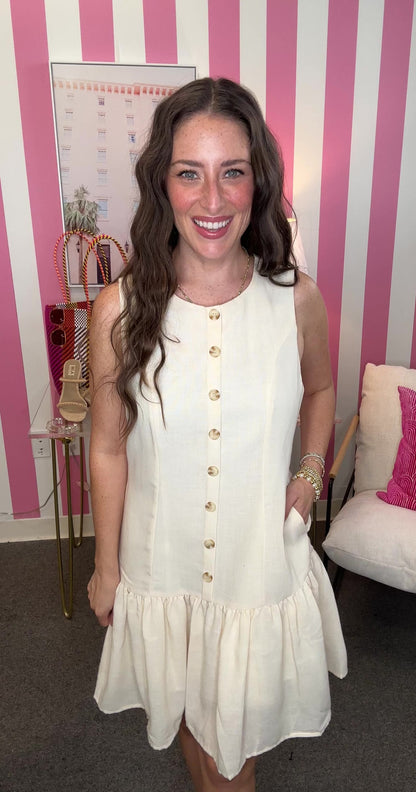 Woman wearing a white dress with gold buttons in a room with pink and white striped walls.