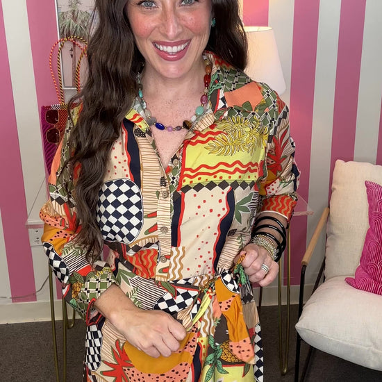 Woman wearing a colorful patterned dress in an indoor setting with pink and white striped walls.
