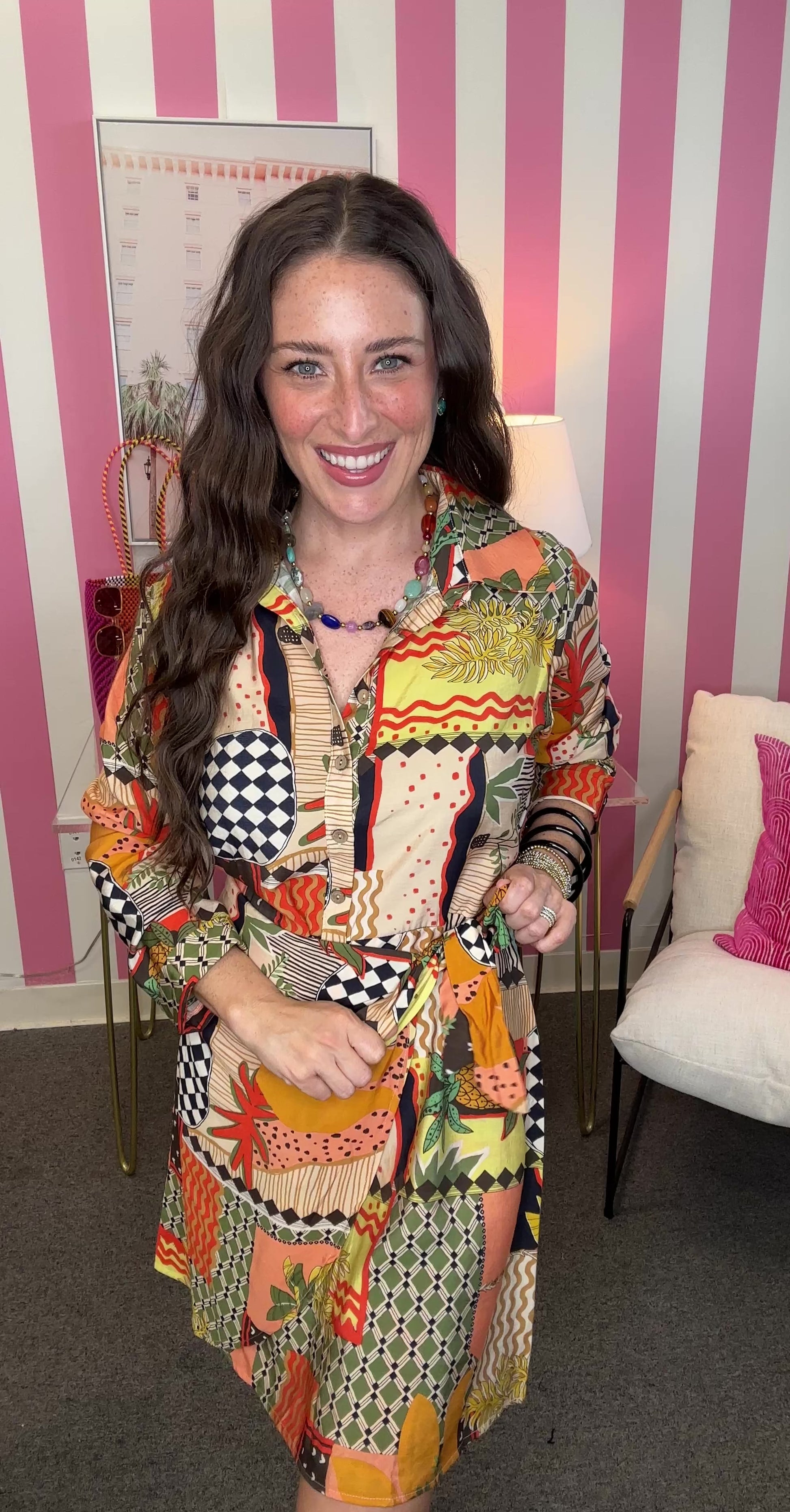 Woman wearing a colorful patterned dress in an indoor setting with pink and white striped walls.