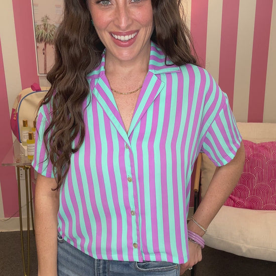 Woman wearing a purple and white striped shirt with jeans in a room with pink and white striped walls.