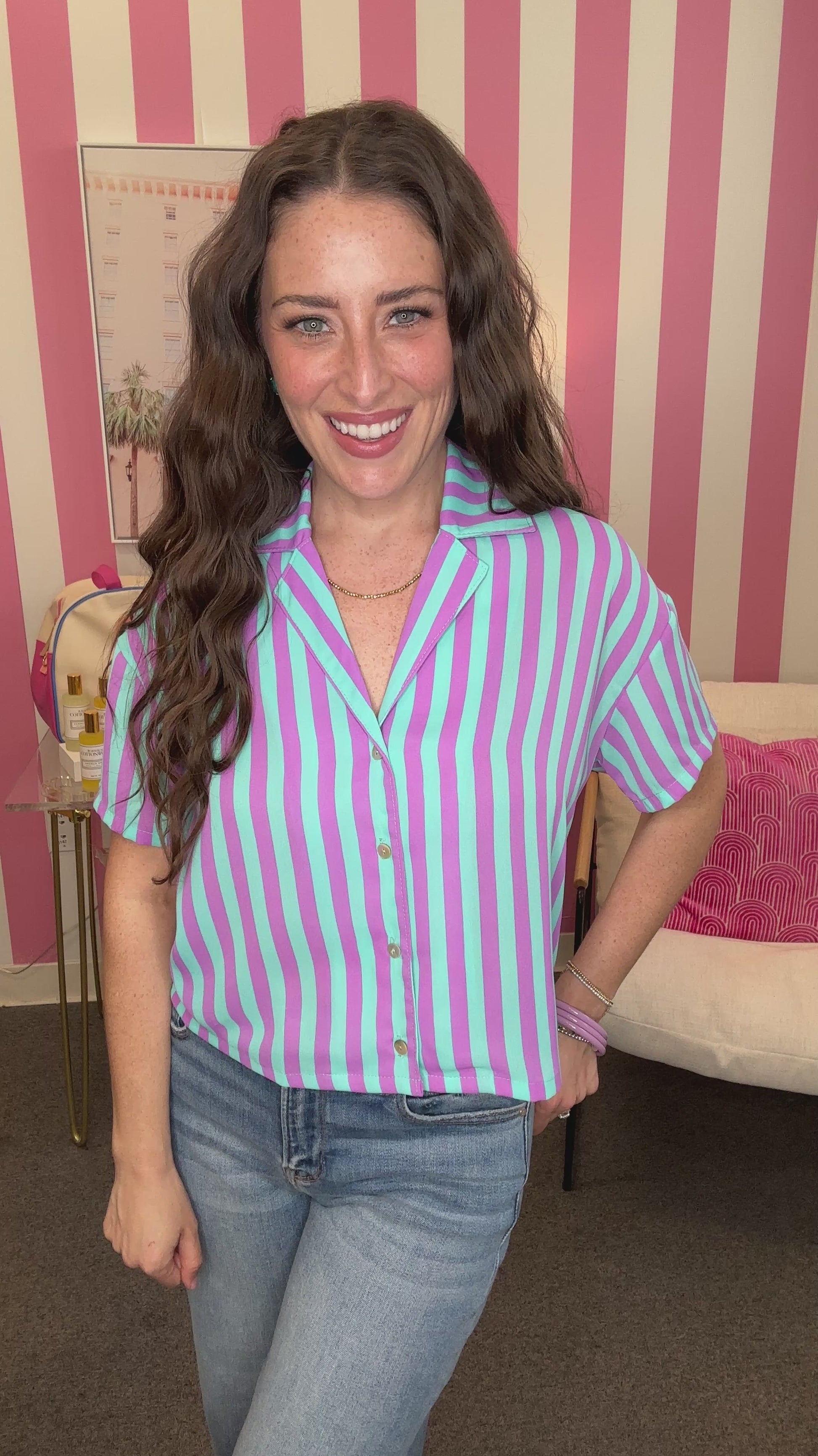 Woman wearing a purple and white striped shirt with jeans in a room with pink and white striped walls.