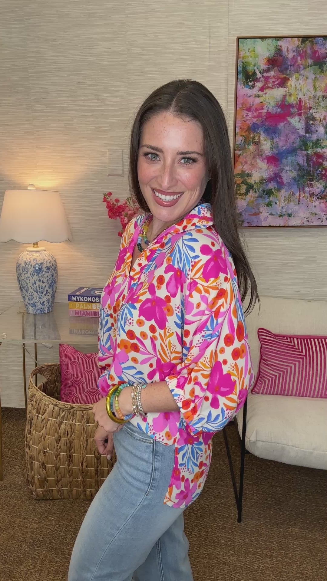 Woman wearing a colorful floral hoodie in a room with a lamp and painting in the background.