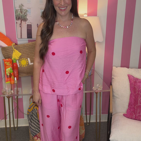Woman in a pink outfit with red polka dots standing in a room with striped walls.