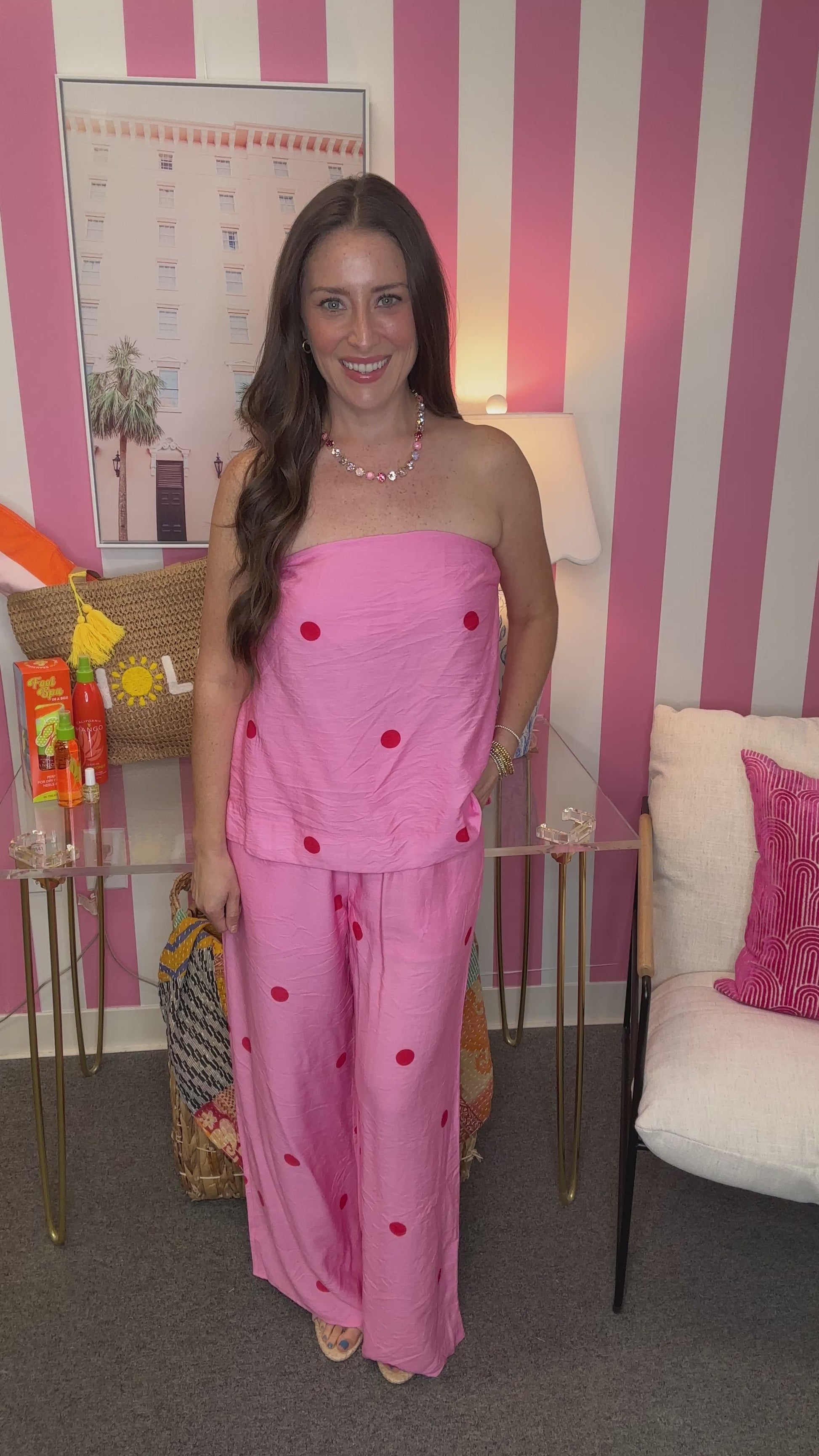 Woman in a pink outfit with red polka dots standing in a room with striped walls.