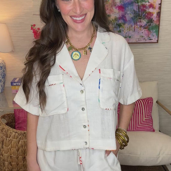 Woman wearing a white outfit with colorful trim in a room with a colorful painting on the wall.