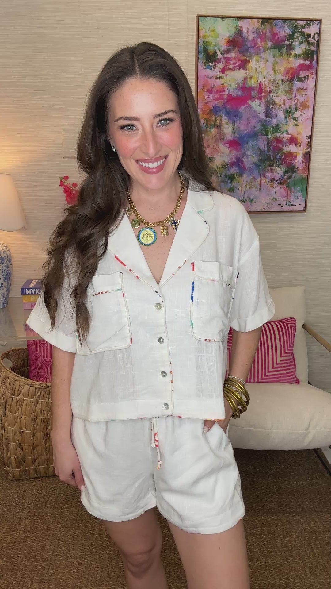 Woman wearing a white outfit with colorful trim in a room with a colorful painting on the wall.