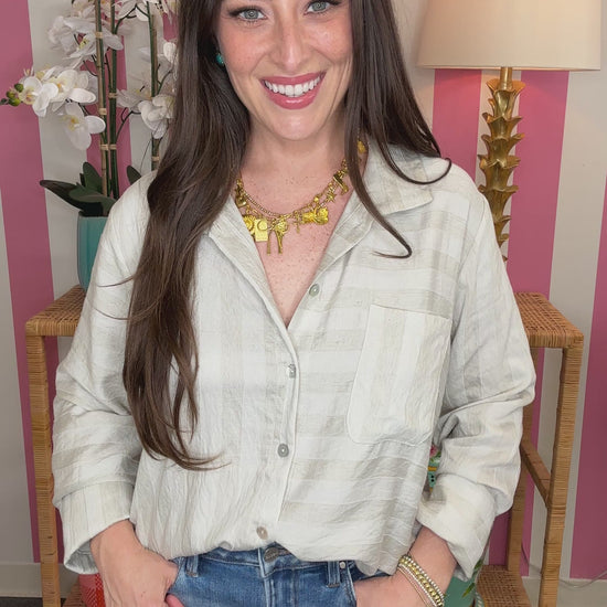 Woman wearing a light-colored shirt and blue jeans in front of a striped wall.