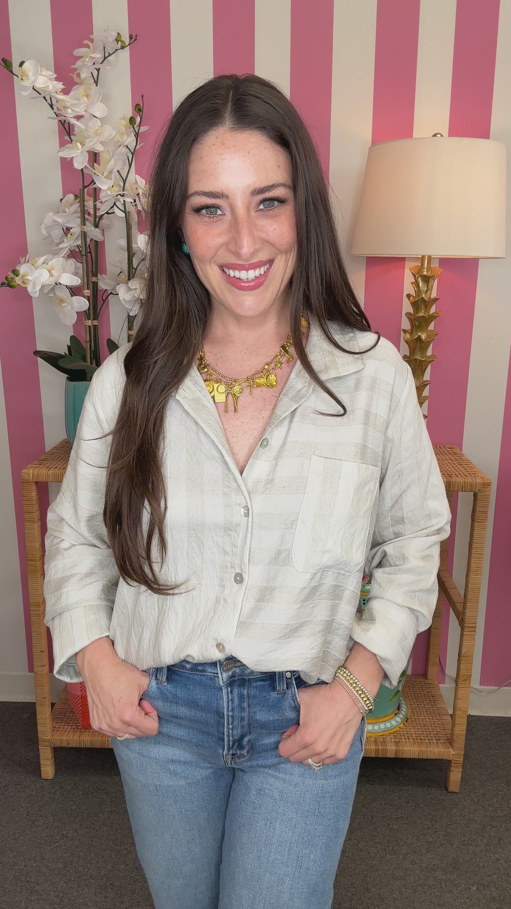 Woman wearing a light-colored shirt and blue jeans in front of a striped wall.
