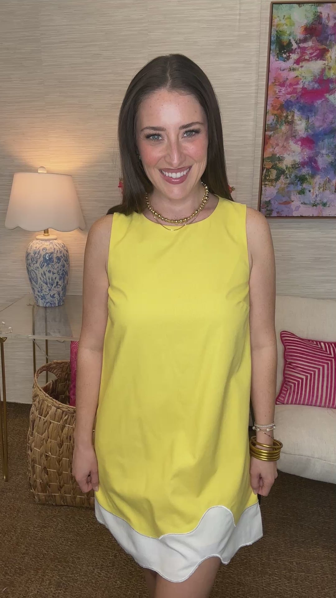 Woman in a yellow dress standing in a living room with a lamp and colorful painting in the background.
