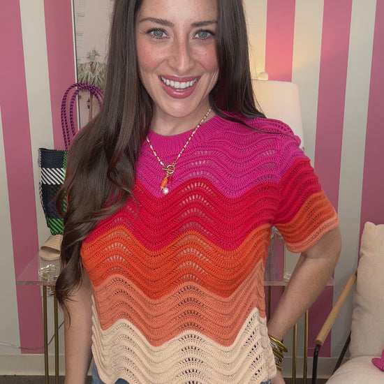 Woman wearing a colorful striped sweater in a room with pink and white striped walls.