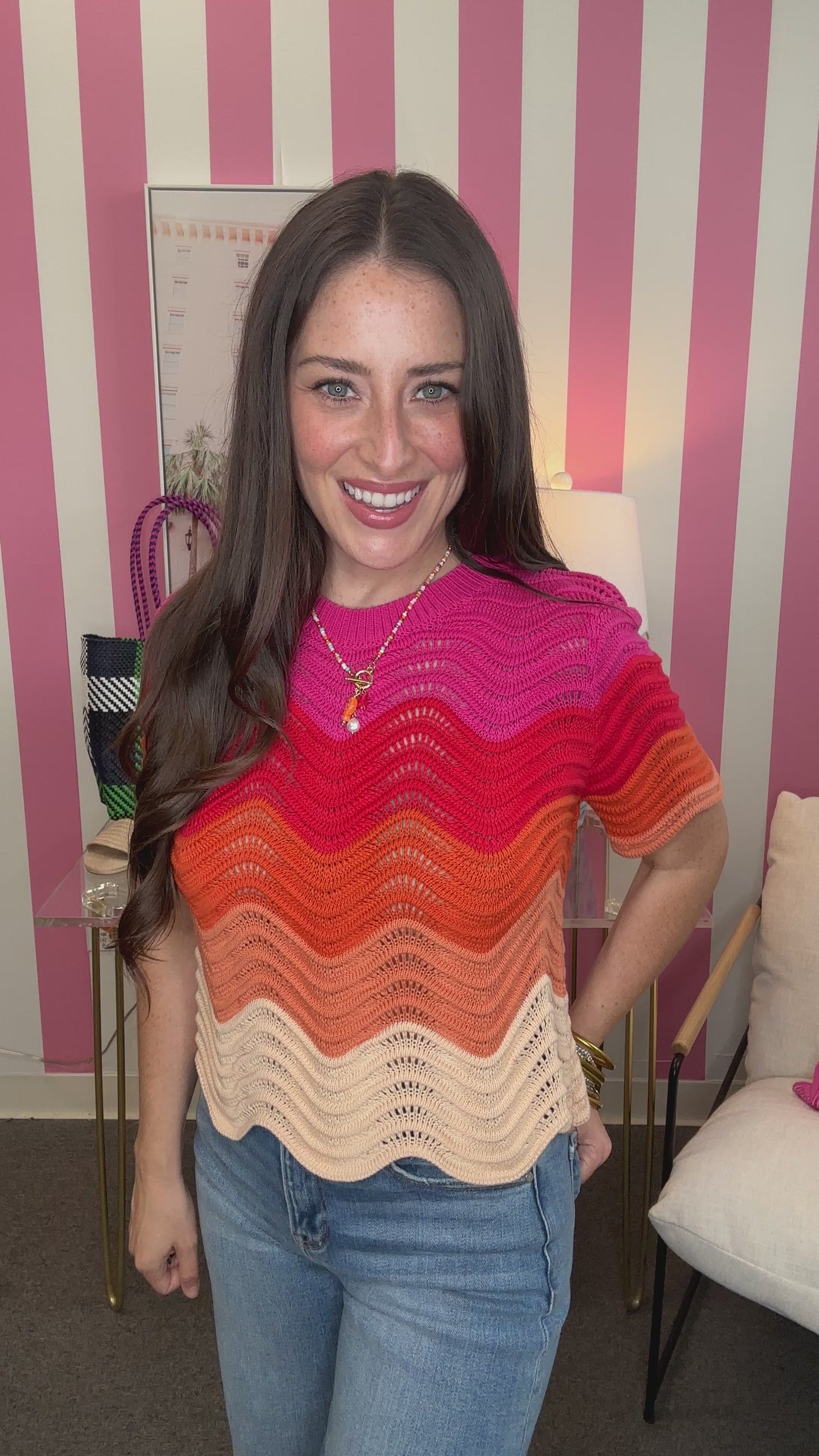 Woman wearing a colorful striped sweater in a room with pink and white striped walls.